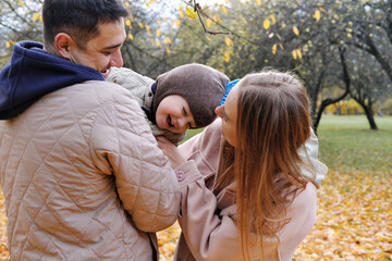 Parents and son spend time together in the autumn park. Father holding son in arms, mother tickling