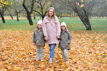 Naklejka premium Caucasian family play in autumn park, mother embrace two girls twins and smile, active weekend outdoors