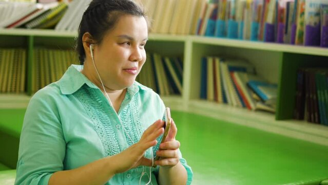 Portrait of Asian woman with blindness disability wearing earphones enjoy using smart phone with voice accessibility for persons with visual impairment disabilities in creative workplace.