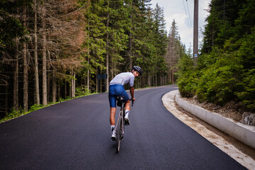 A professional male cyclist is riding a bicycle on an empty forest road. Cyclist wearing cycling...