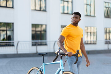 Fototapeta na wymiar Dark skinned handsome man walking street near bicycle while looking away