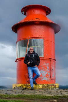 middle aged man photographer posing with camera in front of a red lighthouse