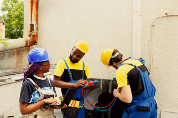 Smiling technicians happy with freon levels in outdoor air conditioner while using manifold gauges...