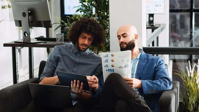 Colleagues review annual statistics in coworking space, analyzing data to create presentation for investment plan. Company workers collaborating on research for executive project. Handheld shot.