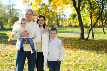 Fototapeta premium A happy family of four spend time in the autumn park. Family smiling and looking at the camera