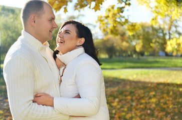 Fototapeta premium Husband and wife on a walk in the autumn park. Husband hugs his wife, and she laughs