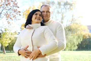 Husband and wife on a walk in the autumn park. Husband hugs his wife, and she laughs