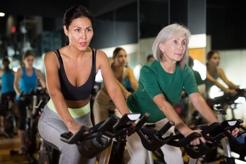 Fototapeta na wymiar Young and adult confident female warming up on bikes in cycling class at gym