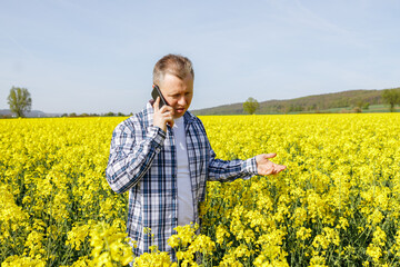 A male farmer agronomist stands in a field of flowering rapeseed and talks on the phone. Checking the quality of the harvest. harvesting.