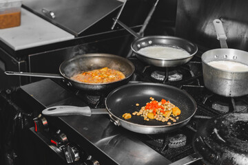 Two cooking pan with risotto on top of the stove and some other mixed ingredients