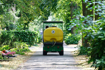 a small van with a large water tank for irrigation drives on a small path of a cemetery in summer
