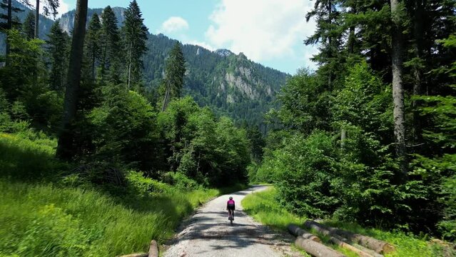 A female cyclist is riding her gravel bicycle on a gravel road between mountains.Sport cycling motivation drone video.