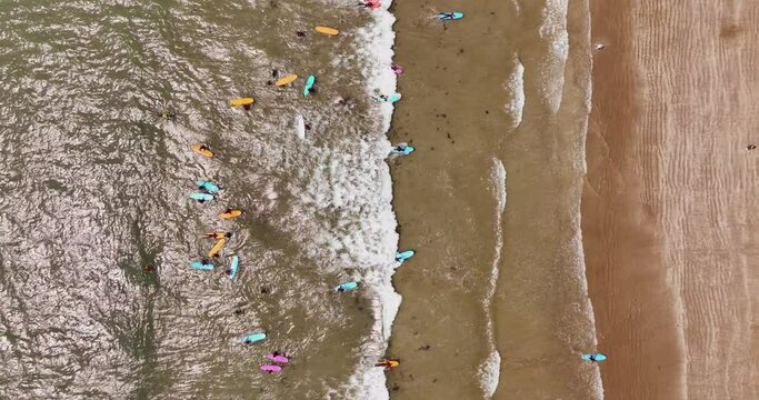 View from above of a beach with surfers practising in the waves by the sand 4k