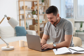 Fototapeta premium Happy man working on laptop at wooden desk in room
