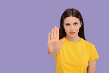 Woman showing stop gesture on violet background. Space for text