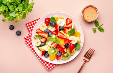 Summer fruit and berry salad with fresh strawberries, blueberries, banana, kiwi, orange and mint, pink background, top view