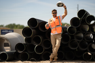 Worker in helmet on break near sewerage pipes. Engineer worker in builder uniform. Portrait of...