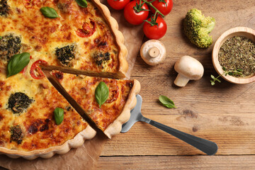 Taking piece of delicious homemade vegetable quiche and ingredients on wooden table, flat lay