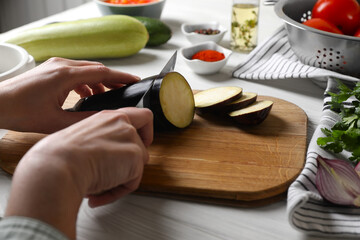 Cooking delicious ratatouille. Woman cutting fresh eggplant at white wooden table, closeup