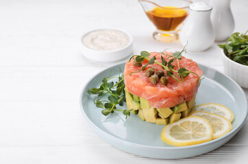 Tasty salmon tartare with avocado, lemon, capers and microgreens on white wooden table. Space for text