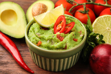 Bowl of delicious guacamole and ingredients on wooden table, closeup