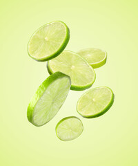 Fresh lime slices falling on light green background
