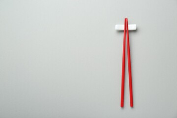 Pair of red chopsticks with rest on light grey background, top view. Space for text
