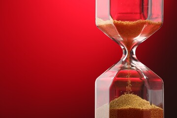 Hourglass with flowing sand on red background, closeup. Space for text
