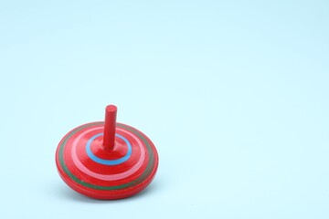 Fototapeta na wymiar One bright spinning top on light blue background, space for text. Toy whirligig
