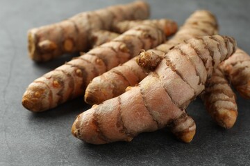 Many raw turmeric roots on grey table, closeup