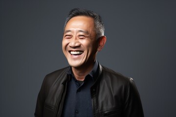 Fototapeta premium Portrait of a happy mature asian man laughing on grey background