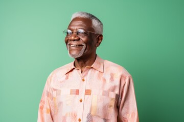 Fototapeta premium Portrait of happy senior Indian man in eyeglasses standing against green background
