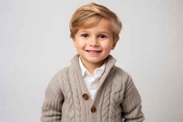 smiling little boy in warm sweater looking at camera isolated on grey