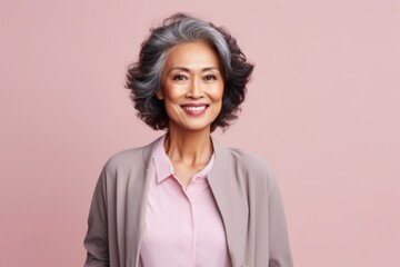 Fototapeta premium Portrait of smiling mature Asian businesswoman standing against pink background.