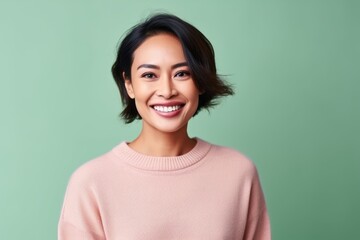 Fototapeta premium Portrait of a beautiful young asian woman smiling and looking at camera isolated over green background