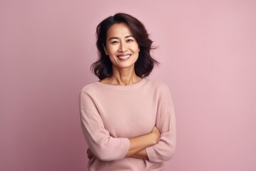 Fototapeta premium Smiling asian woman with crossed arms looking at camera over pink background