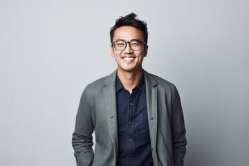 Portrait of a smiling asian man in eyeglasses standing against grey background