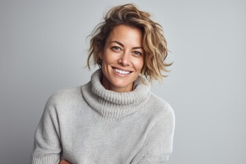 Portrait of a smiling woman in sweater looking at camera over grey background