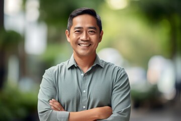 portrait of smiling asian man with arms crossed at city street