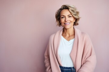 Obraz premium Portrait of a beautiful middle-aged woman with blond hair, wearing a pink sweater, looking at the camera and smiling, on a pink background