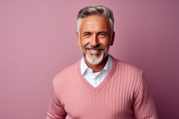 Fototapeta premium Positive senior man looking at camera and smiling while standing against pink background