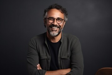 Fototapeta premium Portrait of a handsome Indian man wearing glasses, smiling and looking at camera while standing against black background