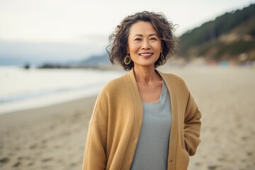 Portrait of smiling middle aged woman standing on beach with arms crossed