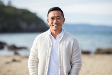 Portrait of smiling asian man standing on beach with ocean in background