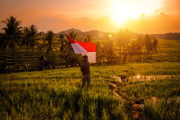 Photo of a village boy waving the Indonesian flag in the middle of a rice field with the silhouette...