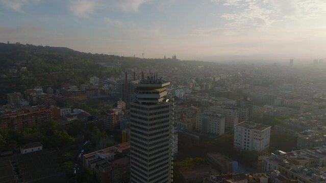 Orbit shot around Edifici Colon. High rise office building towering above surrounding town development. Skyscraper at sunset. Barcelona, Spain