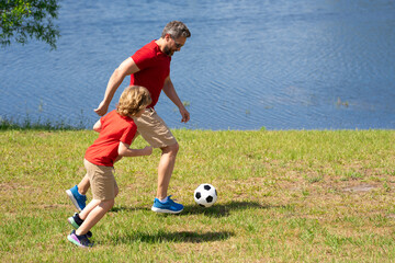Father and son enjoy a friendly game of football. Practice passing and kicking soccer ball. Father teaches his son play football. Family sporty teamwork. Fathers day. Father teaches son play football.