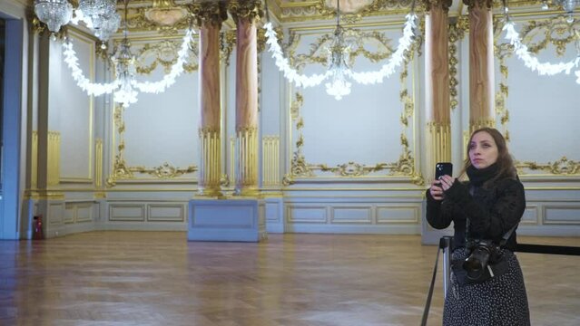 Latina woman blogger broadcasting online on social media and shooting video on smartphone and  photo camera while standing in Orsay Museum in Paris, France on weekend