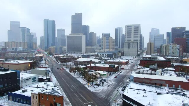 Aerial cinematic drone downtown Denver Colorado city buildings snowing freezing cold winter day gray bird dramatic city landscape car traffic passing cross intersection forward movement