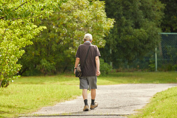 Fototapeta premium 真夏の公園で散歩しているシニア男性の後姿